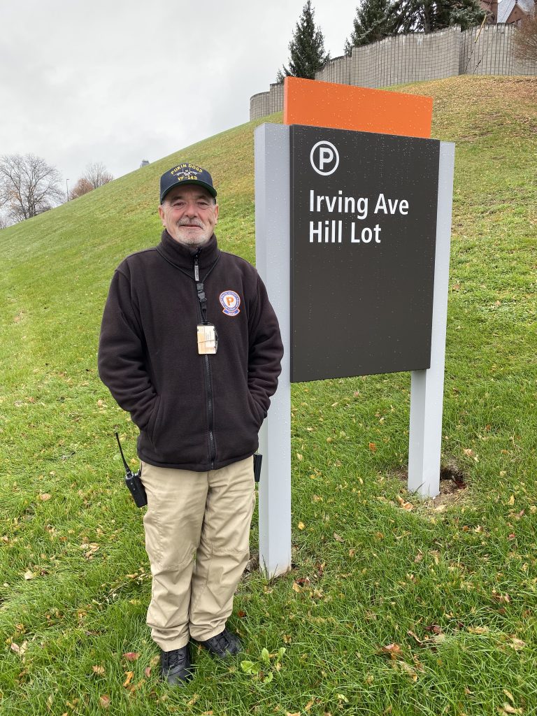 Man Standing Next To Irving Ave. Hill Lot Sign