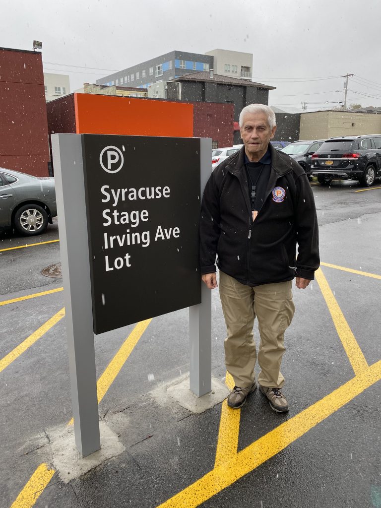 Man Standing Next To Syracuse Stage Irving Ave Lot Sign